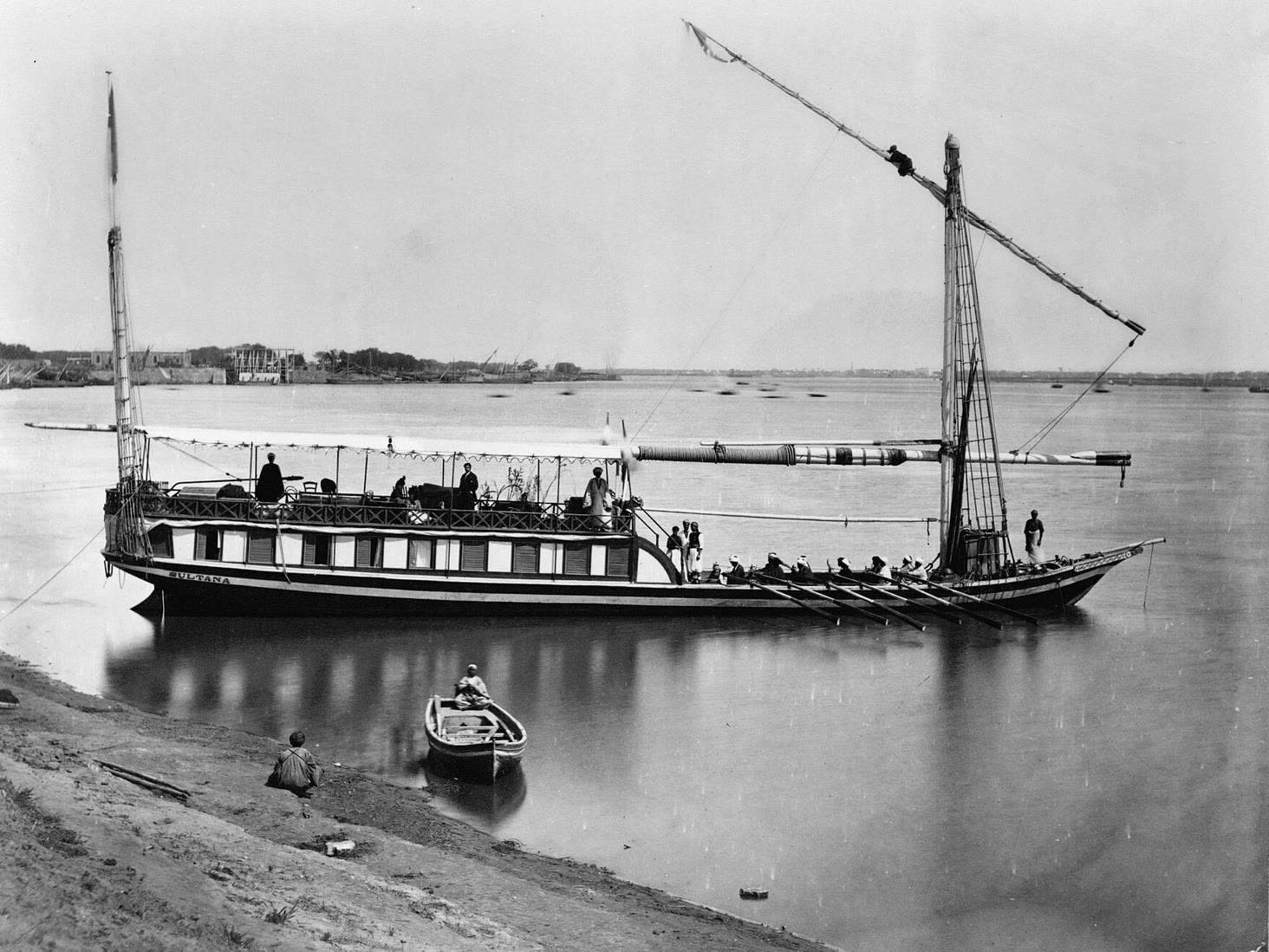 Une dahabiya au grand mât sur une eau calme, une barque au premier plan